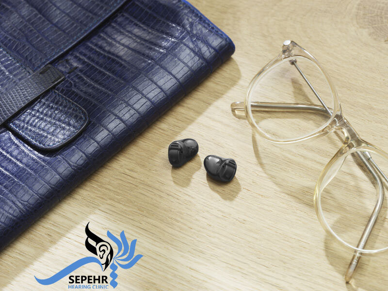 سمعک داخل کانل گوش یا CIC بر روی میز در کنار عینک و کیف